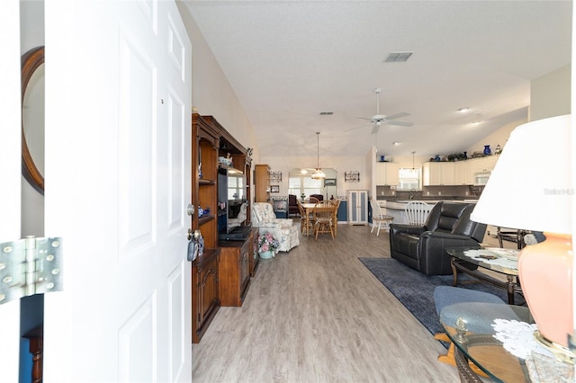 living room with ceiling fan, light hardwood / wood-style flooring, and vaulted ceiling