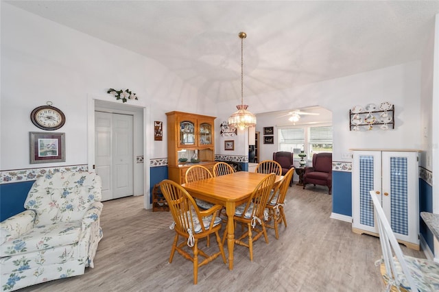 dining room featuring ceiling fan with notable chandelier, lofted ceiling, and light hardwood / wood-style flooring