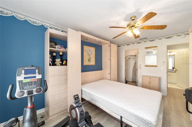 bedroom with ceiling fan, a spacious closet, light wood-type flooring, a textured ceiling, and a closet