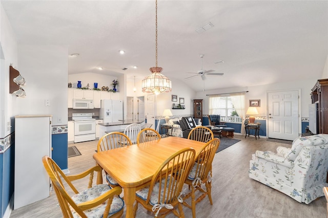 dining room featuring ceiling fan with notable chandelier, light hardwood / wood-style floors, and lofted ceiling