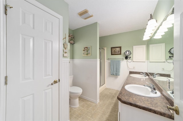 bathroom with vanity, a textured ceiling, toilet, and a shower with door