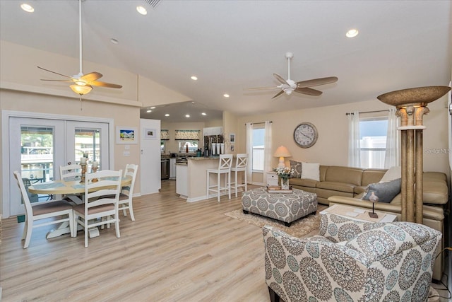 living room with vaulted ceiling, a healthy amount of sunlight, light wood-type flooring, and french doors