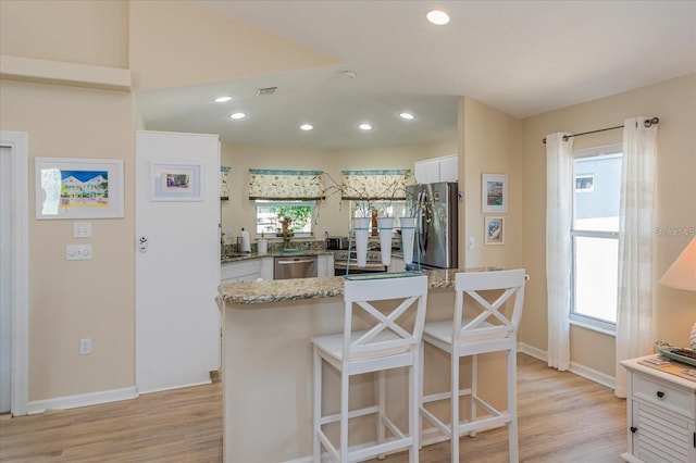 kitchen featuring white cabinetry, appliances with stainless steel finishes, light stone counters, and light hardwood / wood-style flooring