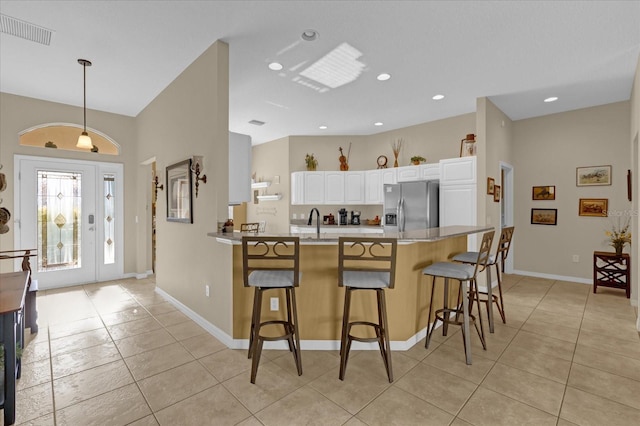 kitchen with a breakfast bar, white cabinets, sink, stainless steel refrigerator with ice dispenser, and light tile patterned floors