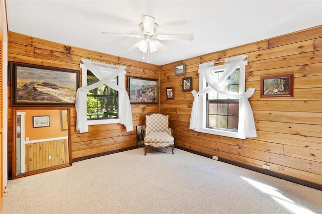 sitting room with wood walls, carpet floors, and ceiling fan