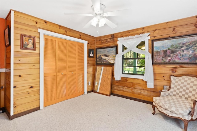 sitting room featuring wood walls, carpet floors, and ceiling fan