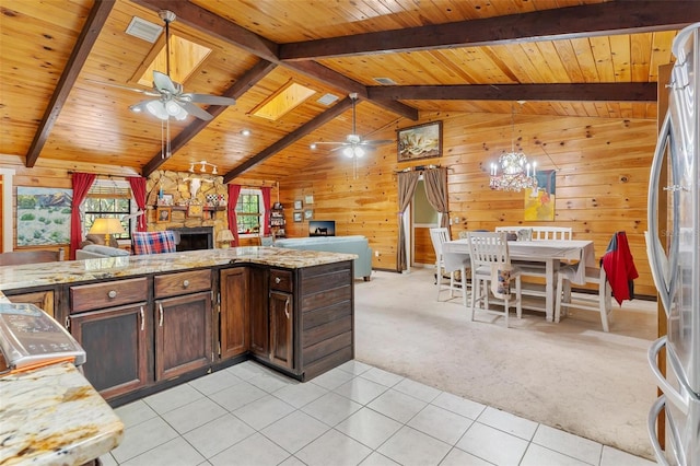 kitchen featuring stainless steel refrigerator, wood walls, lofted ceiling with skylight, decorative light fixtures, and light tile patterned floors