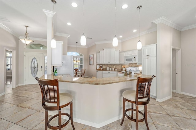 kitchen with white appliances, tasteful backsplash, light stone counters, a kitchen breakfast bar, and a peninsula