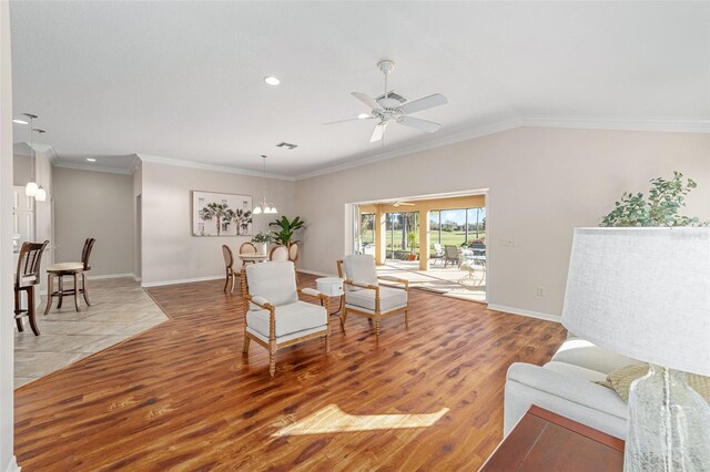 sitting room with light wood-type flooring, ceiling fan with notable chandelier, crown molding, and lofted ceiling