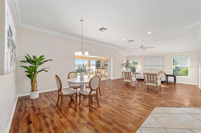 dining space featuring visible vents, lofted ceiling, wood finished floors, crown molding, and ceiling fan with notable chandelier