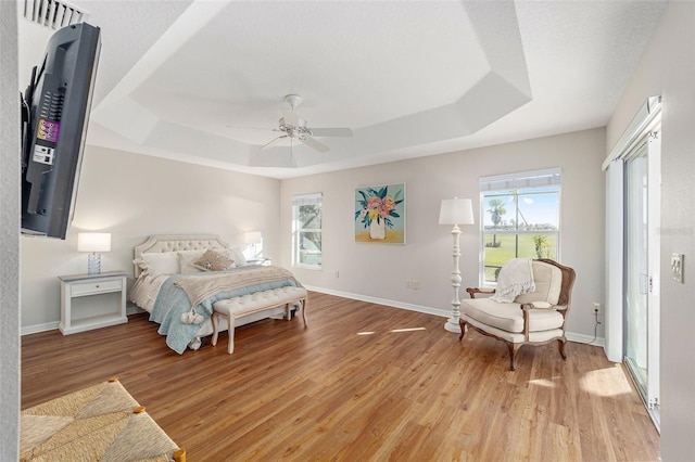 bedroom featuring baseboards, a tray ceiling, and light wood-style floors