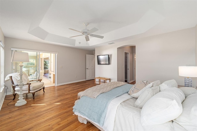 bedroom with arched walkways, visible vents, baseboards, light wood-type flooring, and a raised ceiling