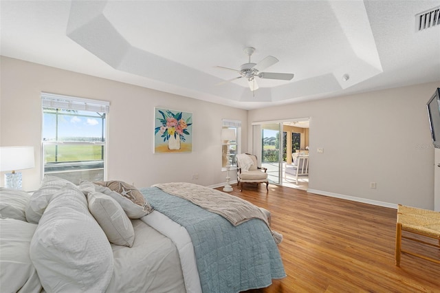 bedroom featuring a tray ceiling, wood finished floors, visible vents, and multiple windows