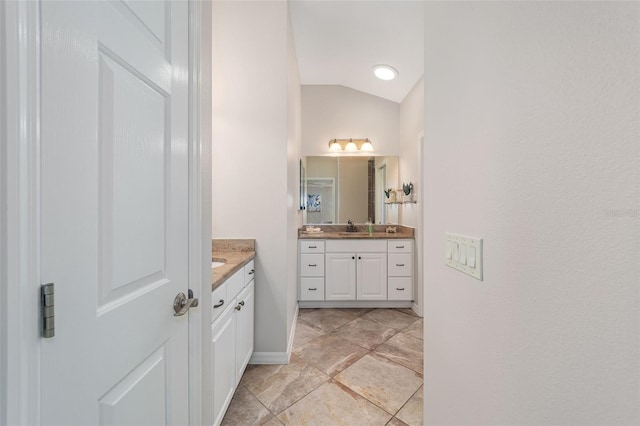 bathroom featuring a sink, baseboards, vaulted ceiling, and two vanities