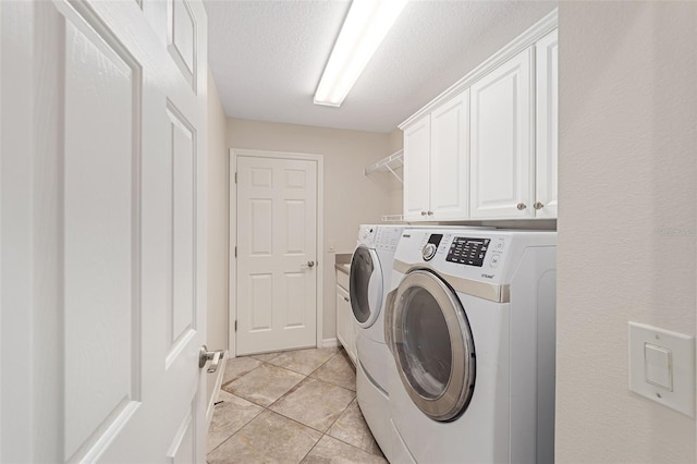 clothes washing area featuring a textured ceiling, light tile patterned floors, baseboards, cabinet space, and washer and clothes dryer