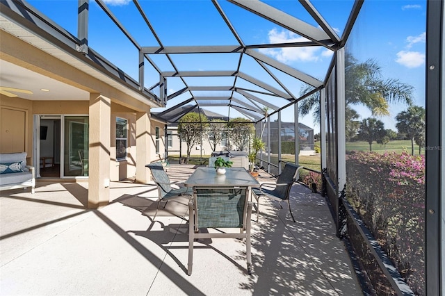 view of patio with a ceiling fan, outdoor dining area, and glass enclosure