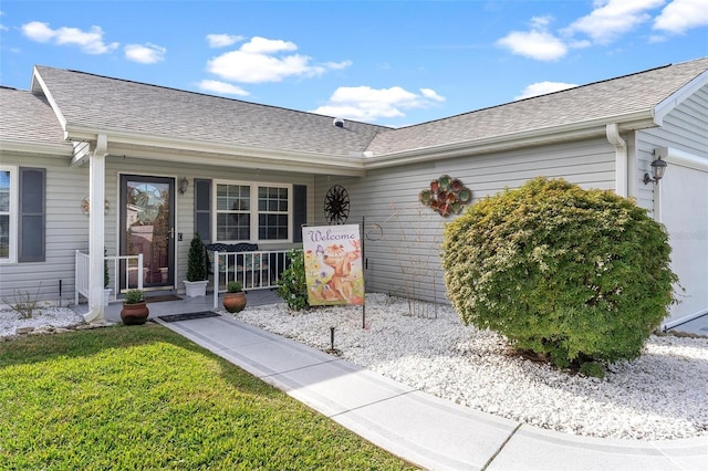 view of exterior entry with a lawn, covered porch, an attached garage, and a shingled roof