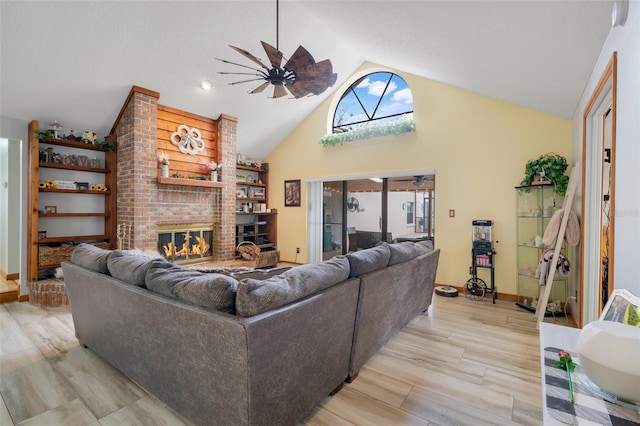 living room featuring a brick fireplace, light wood-type flooring, high vaulted ceiling, and ceiling fan