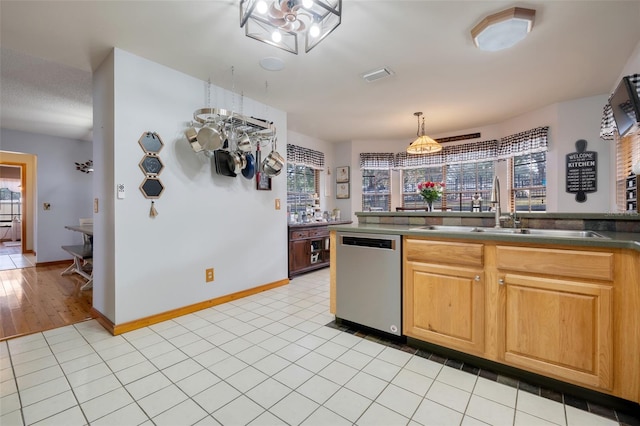 kitchen with light tile patterned flooring, stainless steel dishwasher, decorative light fixtures, and sink