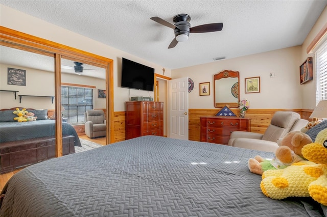 bedroom with multiple windows, ceiling fan, wooden walls, and a textured ceiling