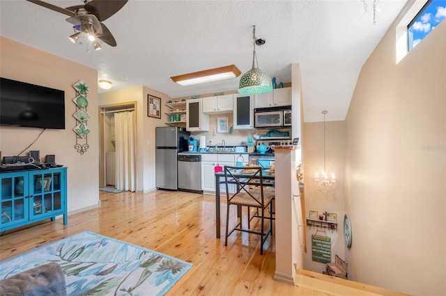 kitchen with white cabinetry, hanging light fixtures, stainless steel appliances, light hardwood / wood-style floors, and a textured ceiling