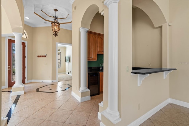 tiled entrance foyer with wine cooler, ornamental molding, a raised ceiling, and decorative columns