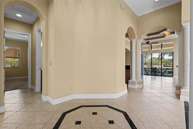 corridor featuring light tile patterned floors, a towering ceiling, ornamental molding, and decorative columns