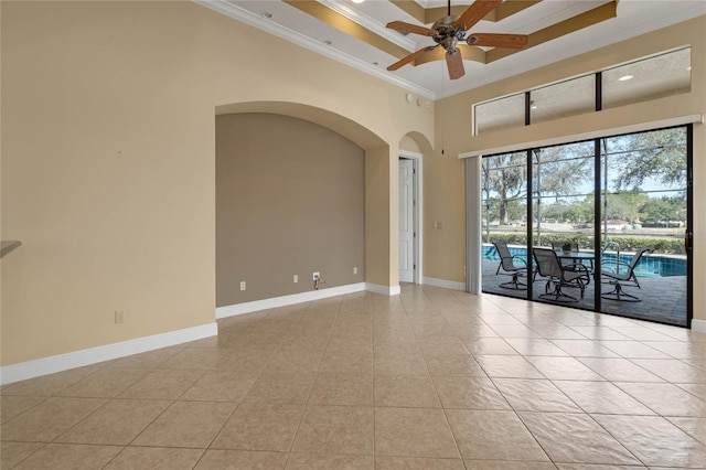 tiled empty room with ceiling fan, ornamental molding, a raised ceiling, and a high ceiling