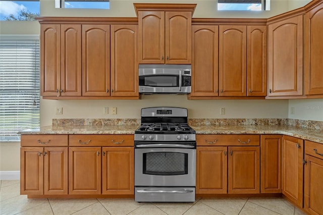 kitchen with stainless steel appliances, a healthy amount of sunlight, light tile patterned floors, and light stone counters