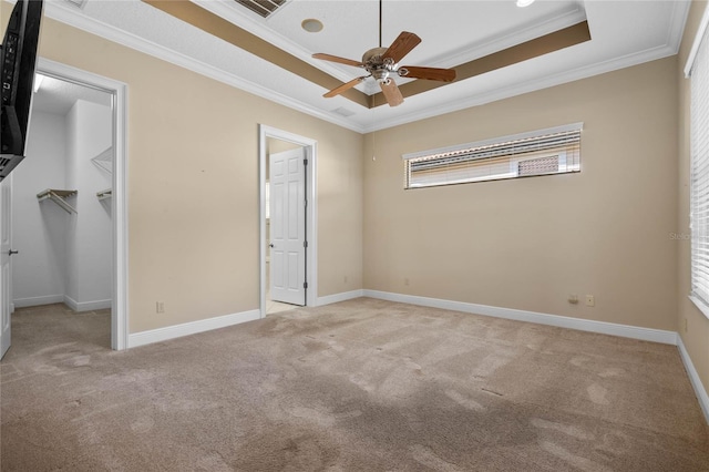 unfurnished bedroom with light carpet, a tray ceiling, ornamental molding, and a spacious closet