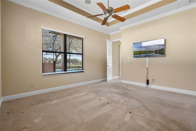 empty room with a raised ceiling, crown molding, light carpet, and ceiling fan