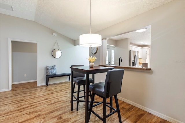 dining room with sink, lofted ceiling, a textured ceiling, and light hardwood / wood-style flooring