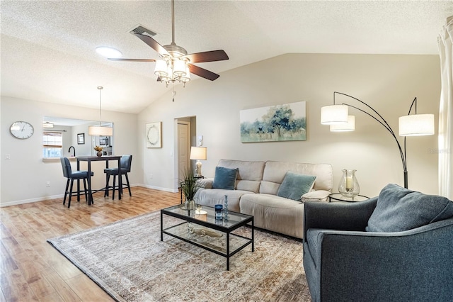 living room featuring a textured ceiling, ceiling fan, vaulted ceiling, and light hardwood / wood-style floors