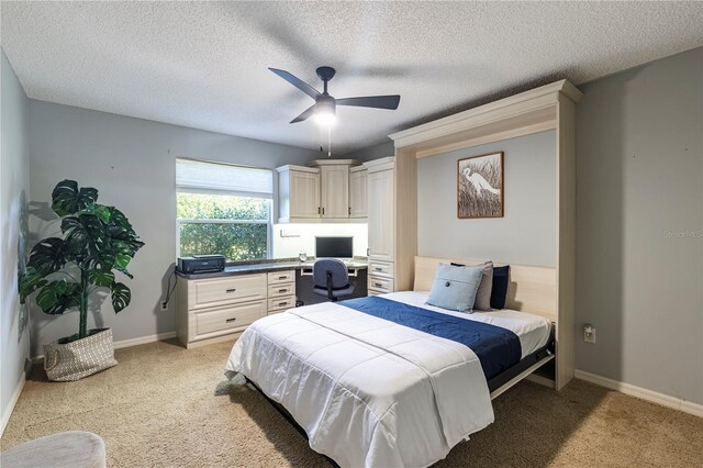 carpeted bedroom with ceiling fan, built in desk, and a textured ceiling