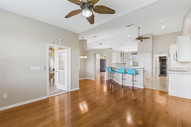 interior space with vaulted ceiling, light wood-style flooring, a kitchen breakfast bar, white cabinetry, and a ceiling fan