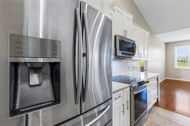 kitchen featuring tasteful backsplash, vaulted ceiling, light tile patterned floors, appliances with stainless steel finishes, and white cabinets