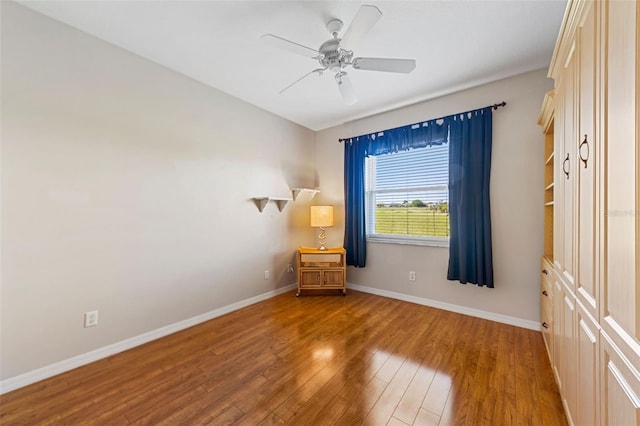 spare room with baseboards, wood finished floors, and a ceiling fan