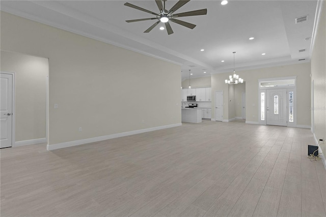 unfurnished living room featuring ceiling fan with notable chandelier, light wood-type flooring, ornamental molding, and a tray ceiling