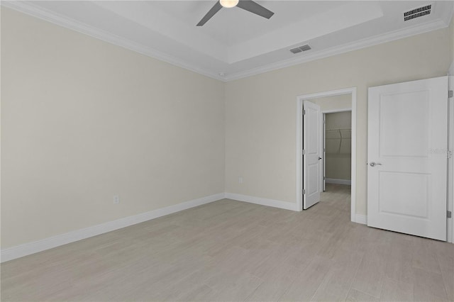 spare room featuring a raised ceiling, ceiling fan, and light wood-type flooring