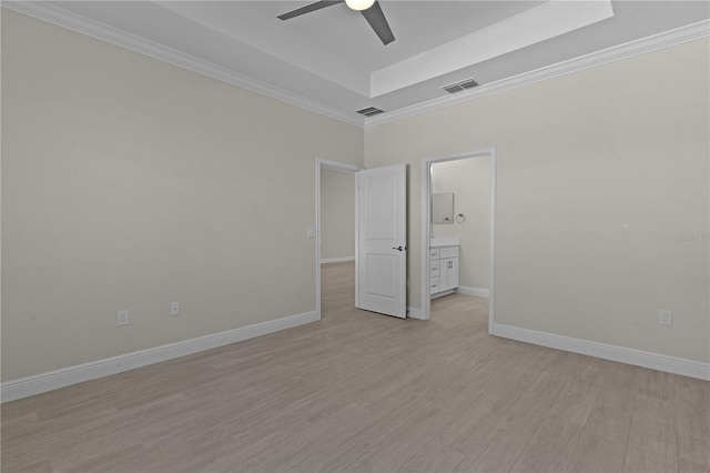 unfurnished bedroom with light wood-type flooring, ensuite bath, a tray ceiling, ceiling fan, and crown molding