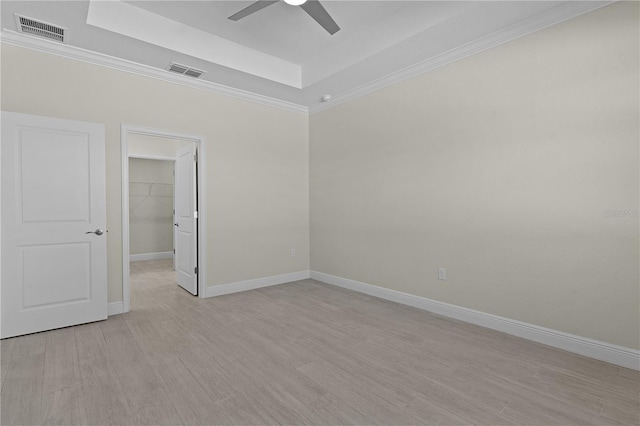 unfurnished room featuring a raised ceiling, ceiling fan, and light wood-type flooring