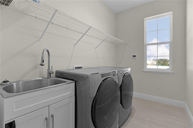 laundry room featuring washer and clothes dryer, light hardwood / wood-style floors, cabinets, and sink