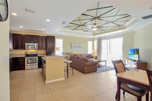 kitchen with a kitchen bar, stainless steel appliances, a raised ceiling, and crown molding