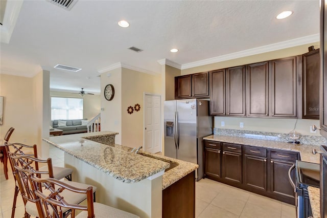 kitchen featuring light stone countertops, ceiling fan, a kitchen breakfast bar, stainless steel fridge with ice dispenser, and a kitchen island with sink