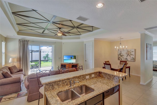 kitchen featuring stainless steel dishwasher, ceiling fan with notable chandelier, a raised ceiling, sink, and an island with sink