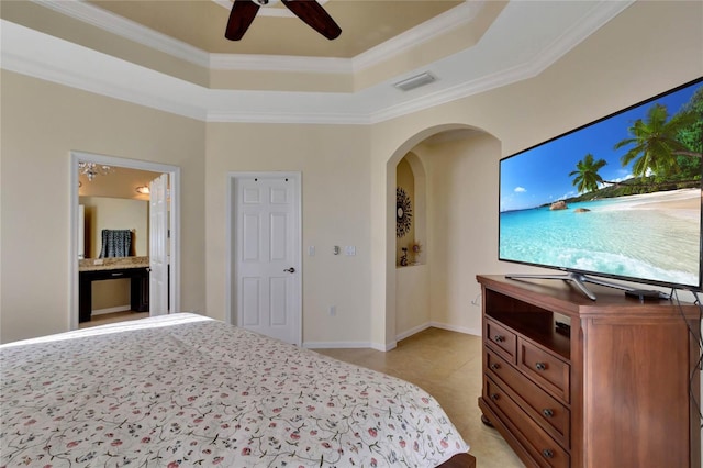 bedroom featuring ceiling fan, ornamental molding, a tray ceiling, and ensuite bath