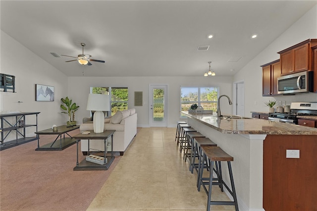 kitchen featuring a kitchen bar, ceiling fan with notable chandelier, stainless steel appliances, sink, and stone counters