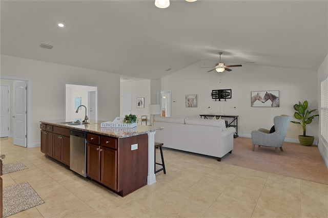 kitchen with ceiling fan, dishwasher, sink, light stone counters, and an island with sink