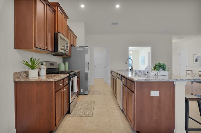 kitchen featuring light stone countertops, sink, stainless steel appliances, a kitchen breakfast bar, and a kitchen island with sink