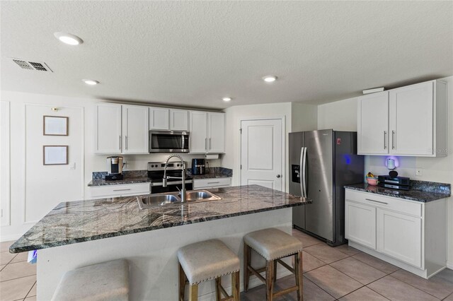 kitchen featuring a kitchen island with sink, sink, light tile patterned flooring, white cabinetry, and stainless steel appliances